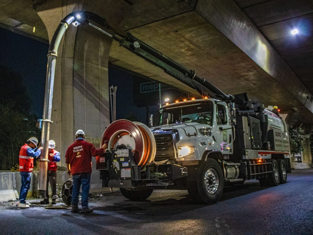 Street workers cleaning drainage at night with machinery, representing field crews using equipment while needing to document